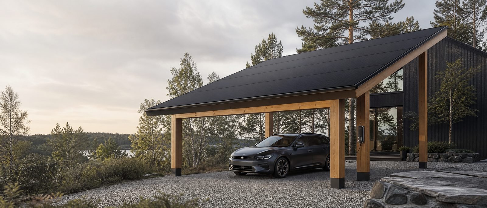 A CAROSOLARO Signature pavilion in glulam timber with a full-black solar roof, beside a dark-clad Northern European house